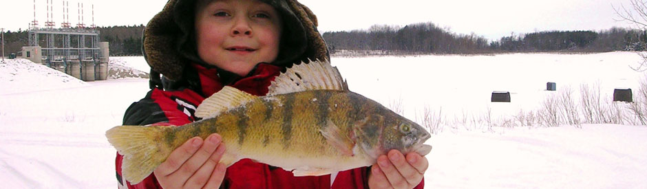 Boy holding a fish with Shand Dam in background, in winter