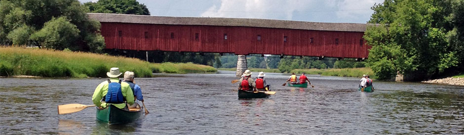 People in canoes along a river under a heritage bridge