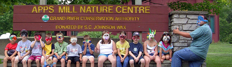 Children wearing masks sitting in front of Apps' Mill Nature Centre sign